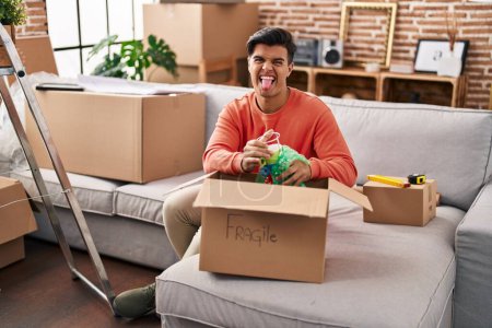 Photo for Hispanic man moving to a new home unpacking sticking tongue out happy with funny expression. - Royalty Free Image