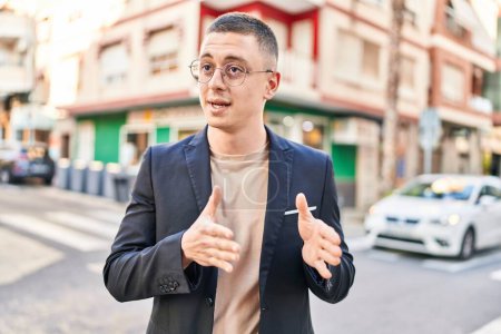 Téléchargez les photos : Jeune homme hispanique exécutif souriant confiant parlant dans la rue - en image libre de droit