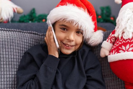 Téléchargez les photos : Adorable garçon hispanique parlant sur smartphone assis sur le canapé par la décoration de Noël à la maison - en image libre de droit