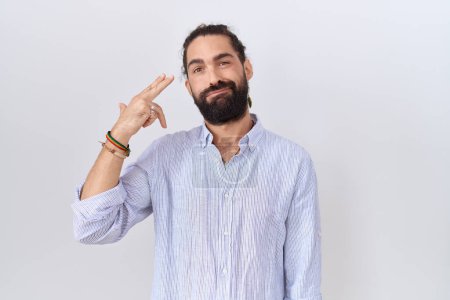 Foto de Hombre hispano con barba vistiendo camisa casual disparándose y matándose apuntando de la mano y los dedos a la cabeza como arma, gesto suicida. - Imagen libre de derechos