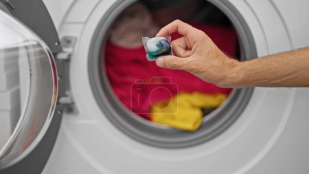 Téléchargez les photos : Jeune homme hispanique mettant sac de détergent sur la machine à laver à la buanderie - en image libre de droit