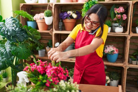 Téléchargez les photos : Young beautiful arab woman florist talking on smartphone cutting plant at flower shop - en image libre de droit