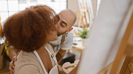 Téléchargez les photos : Deux artistes confiants, partenaires dans l'art et l'amour, souriant et embrassant tout en dessinant à la classe de studio intérieur. - en image libre de droit