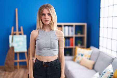 Photo for Blonde caucasian woman standing at living room with serious expression on face. simple and natural looking at the camera. - Royalty Free Image