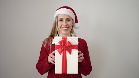 Téléchargez les photos : Jeune femme blonde portant un chapeau de Noël tenant un cadeau sur fond blanc isolé - en image libre de droit