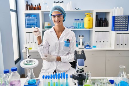Téléchargez les photos : Femme brune travaillant au laboratoire scientifique avec un grand sourire sur le visage, pointant du doigt vers le côté en regardant la caméra. - en image libre de droit