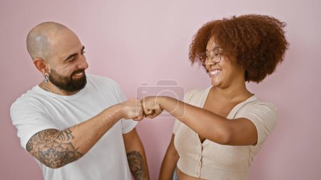 Photo for Beautiful couple standing together, bumping fists in celebration over an isolated pink background, emitting confidence and happiness - Royalty Free Image