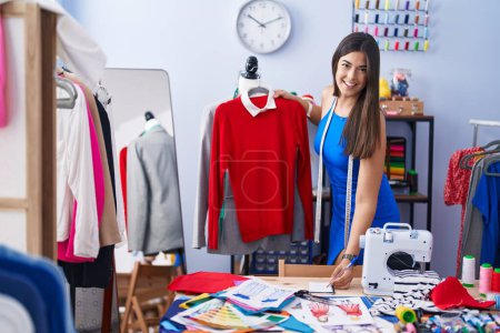 Photo for Young beautiful hispanic woman tailor smiling confident holding t shirt writing on notebook at tailor shop - Royalty Free Image