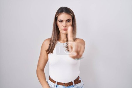 Foto de Mujer joven hispana de pie sobre fondo blanco señalando con el dedo hacia arriba y la expresión enojada, sin mostrar ningún gesto - Imagen libre de derechos
