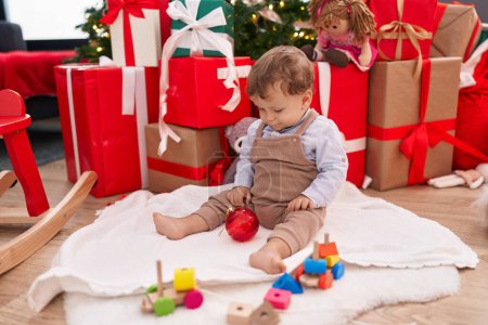 Photo for Adorable blond toddler playing with toys sitting on floor by christmas gifts at home - Royalty Free Image