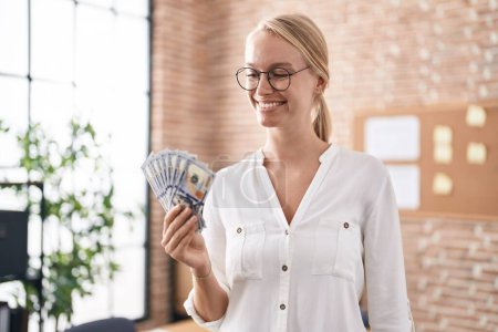 Photo for Young blonde woman business worker holding dollars at office - Royalty Free Image