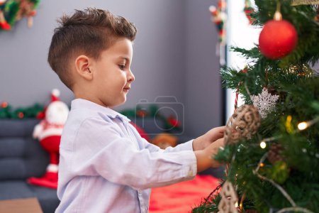 Photo for Adorable hispanic toddler smiling confident decorating christmas tree at home - Royalty Free Image