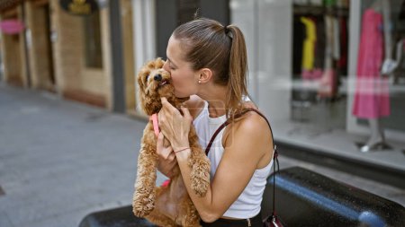 Téléchargez les photos : Jeune femme caucasienne avec chien assis sur un banc embrassant dans la rue - en image libre de droit