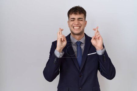 Photo for Young hispanic business man wearing suit and tie gesturing finger crossed smiling with hope and eyes closed. luck and superstitious concept. - Royalty Free Image