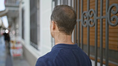 Photo for Handsome, mature hispanic man seen from behind, standing backward on an urban street, immersed in his thoughts while appreciating the city exterior - Royalty Free Image