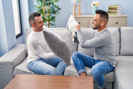 Photo for Two men couple fighting with cushion sitting on sofa at home - Royalty Free Image