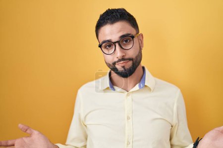 Photo for Hispanic young man wearing business clothes and glasses clueless and confused with open arms, no idea concept. - Royalty Free Image