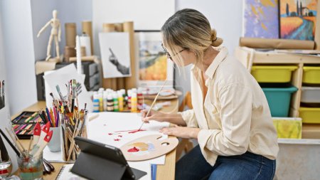 Téléchargez les photos : Jeune artiste blonde dessinant sur papier à l'aide du pavé tactile au studio d'art - en image libre de droit
