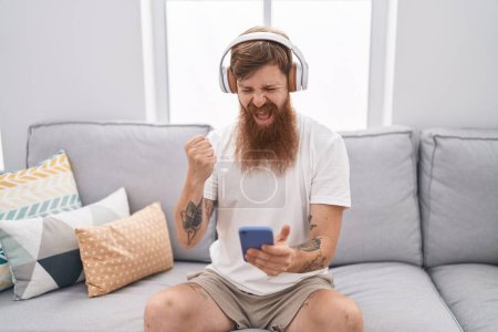 Photo for Young redhead man listening to music sitting on sofa at home - Royalty Free Image