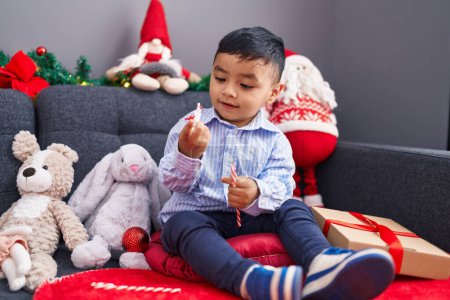 Photo for Adorable hispanic toddler looking christmas star decoration sitting on sofa at home - Royalty Free Image