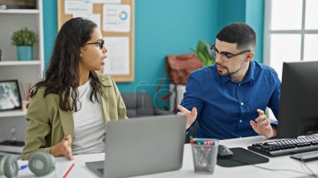 Foto de Dos empleados de oficina, un hombre y una mujer, sentados en una mesa, enredados en una acalorada discusión en su lugar de trabajo - Imagen libre de derechos