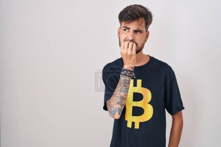 Photo for Young hispanic man with tattoos wearing bitcoin t shirt looking stressed and nervous with hands on mouth biting nails. anxiety problem. - Royalty Free Image
