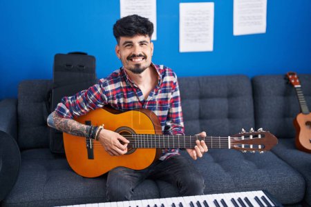 Photo for Young hispanic man artist smiling confident playing classical guitar at music studio - Royalty Free Image