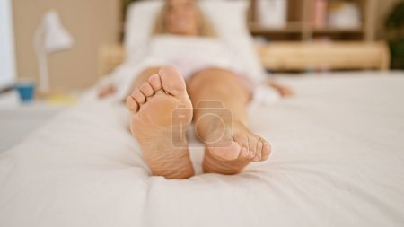 Foto de Mujer rubia joven acostada en la cama moviendo los pies en el dormitorio - Imagen libre de derechos