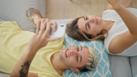 Téléchargez les photos : Beau couple utilisant des smartphones couchés sur le canapé à la maison - en image libre de droit