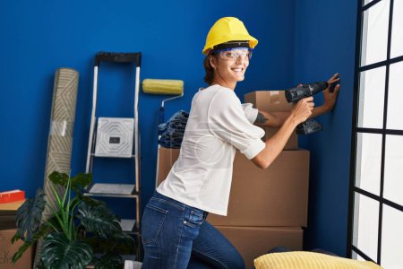 Photo for Young beautiful hispanic woman smiling confident drilling wall at new home - Royalty Free Image