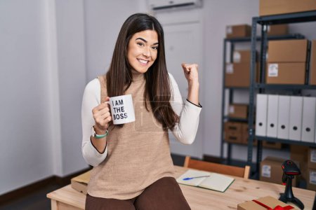 Photo for Young brunette woman working at small business ecommerce holding i am the boss cup screaming proud, celebrating victory and success very excited with raised arm - Royalty Free Image
