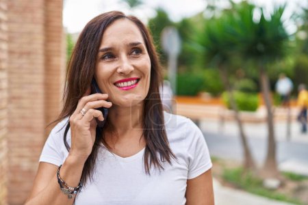 Foto de Joven hermosa mujer hispana sonriendo confiada hablando en el teléfono inteligente en la calle - Imagen libre de derechos