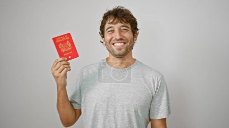 Téléchargez les photos : Rayonnant jeune homme présente joyeusement son laissez-passer, un passeport singapore, en toute confiance debout isolé sur un fond blanc - en image libre de droit