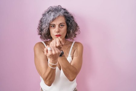 Photo for Middle age woman with grey hair standing over pink background ready to fight with fist defense gesture, angry and upset face, afraid of problem - Royalty Free Image