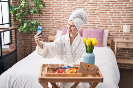 Foto de Mujer rubia joven hacer selfie por teléfono inteligente desayunando en el dormitorio - Imagen libre de derechos