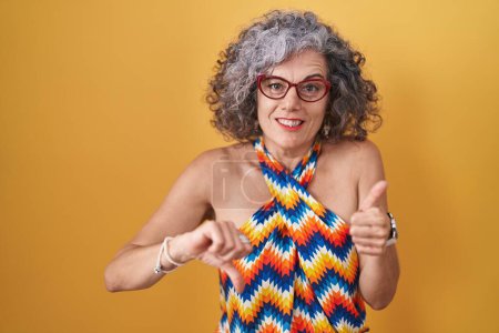 Photo for Middle age woman with grey hair standing over yellow background doing thumbs up and down, disagreement and agreement expression. crazy conflict - Royalty Free Image