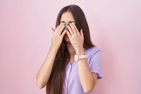 Téléchargez les photos : Jeune femme hispanique avec les cheveux longs debout sur fond rose frottant les yeux pour la fatigue et les maux de tête, somnolent et l'expression fatiguée. problème de vision - en image libre de droit