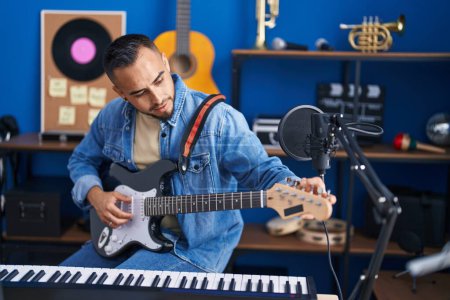 Foto de Joven músico hispano tocando la guitarra eléctrica en el estudio de música - Imagen libre de derechos