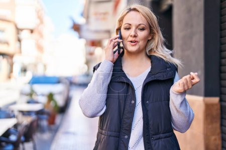Photo for Young blonde woman smiling confident talking on the smartphone at street - Royalty Free Image