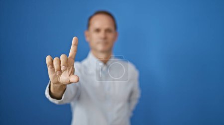Photo for Handsome mature man, in cool casual fashion, seriously gesturing 'no' with his finger, standing isolated against a stark white background. concentrated expression, yet appears relaxed. - Royalty Free Image