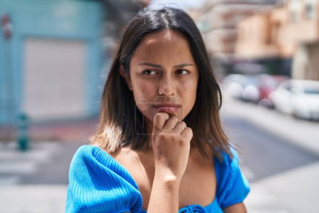 Téléchargez les photos : Jeune femme hispanique debout avec l'expression du doute dans la rue - en image libre de droit