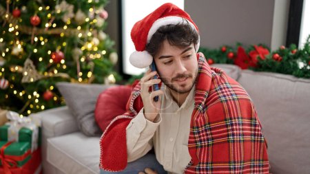 Foto de Joven hombre hispano celebrando la Navidad hablando en el teléfono inteligente en casa - Imagen libre de derechos