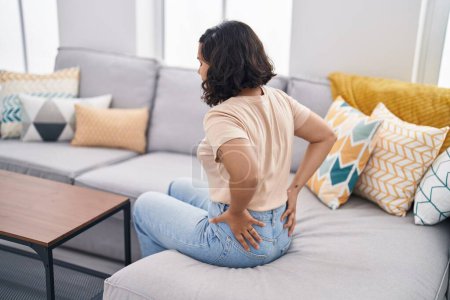Foto de Mujer joven sentada en el sofá sufriendo de dolor de espalda en casa - Imagen libre de derechos