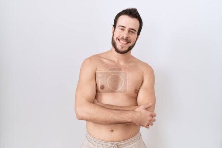 Foto de Joven hombre hispano de pie sin camisa sobre fondo blanco rostro feliz sonriendo con los brazos cruzados mirando a la cámara. persona positiva. - Imagen libre de derechos