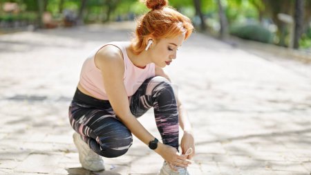 Photo for Young redhead woman wearing sportswear tying shoes at park - Royalty Free Image