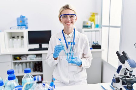 Foto de Joven mujer rubia científica analizando tubos de ensayo en laboratorio - Imagen libre de derechos