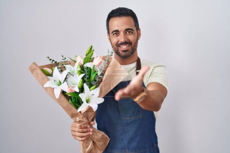 Téléchargez les photos : Homme hispanique avec barbe travaillant comme fleuriste souriant joyeuse offrant la main de la paume donnant assistance et acceptation. - en image libre de droit