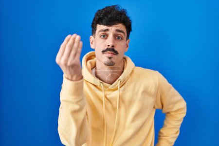 Photo for Hispanic man standing over blue background doing italian gesture with hand and fingers confident expression - Royalty Free Image