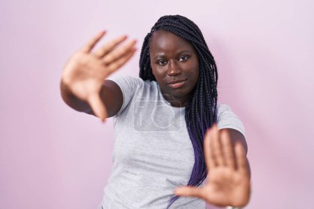 Téléchargez les photos : Jeune femme africaine debout sur fond rose faisant cadre en utilisant les mains paumes et les doigts, perspective de la caméra - en image libre de droit