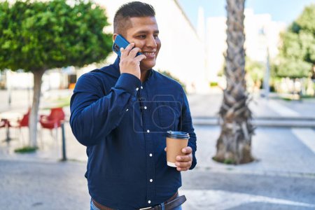 Téléchargez les photos : Jeune homme latino parlant sur smartphone boire du café à la rue - en image libre de droit